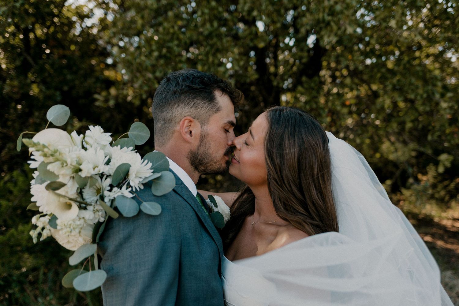 Bride and groom sharing a romantic kiss with white floral bouquet outdoors. Edmond Oklahoma wedding