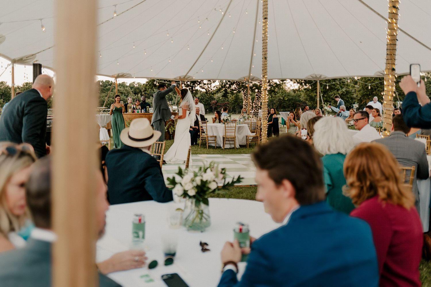 Guests seated at round tables under a sailcloth tent as couple shares first dance at wedding. Oklahoma Spring wedding on a family farm