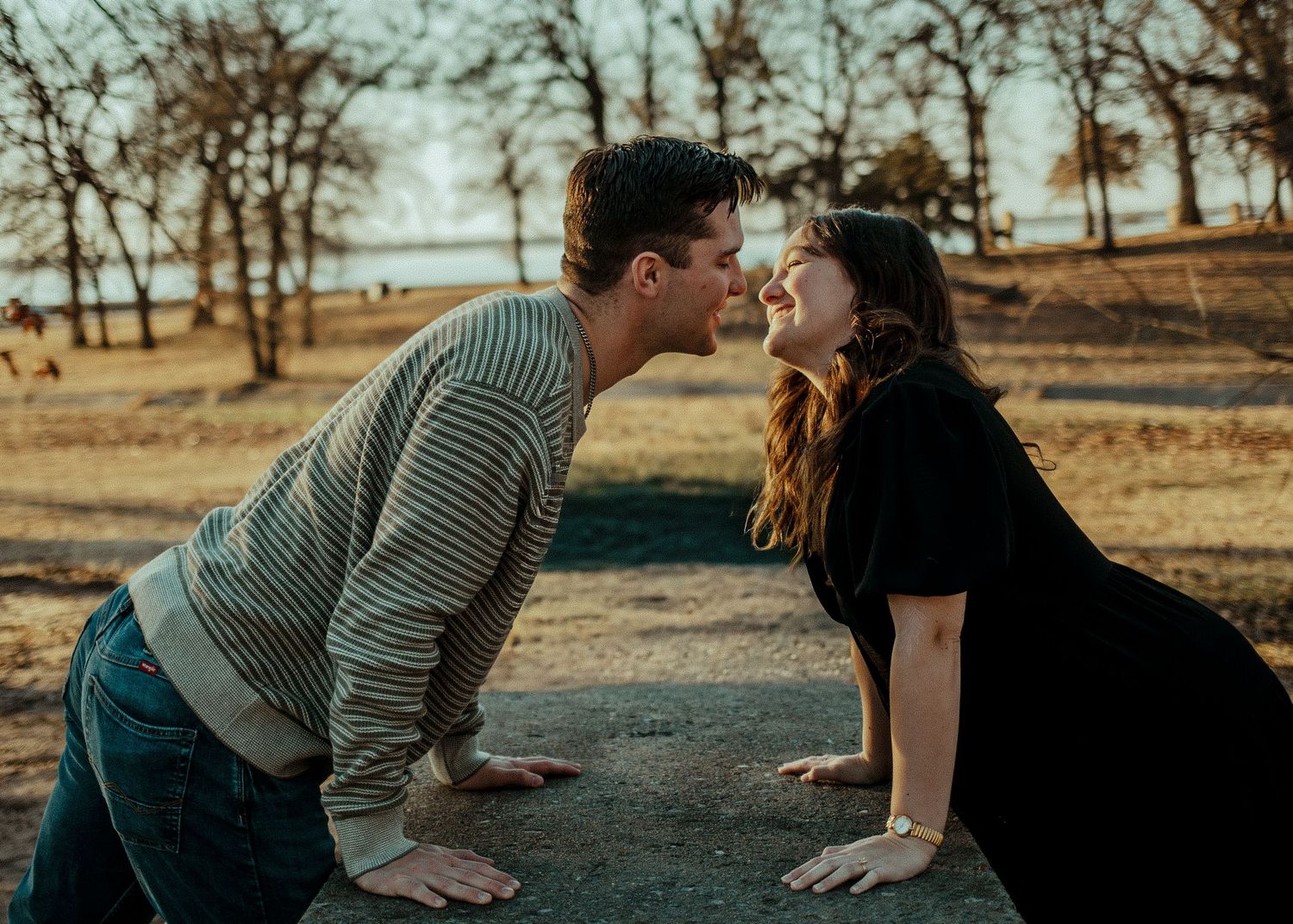 A joyful couple leaning in for a kiss in an autumn park at golden hour. Oklahoma City couple photoshoot.