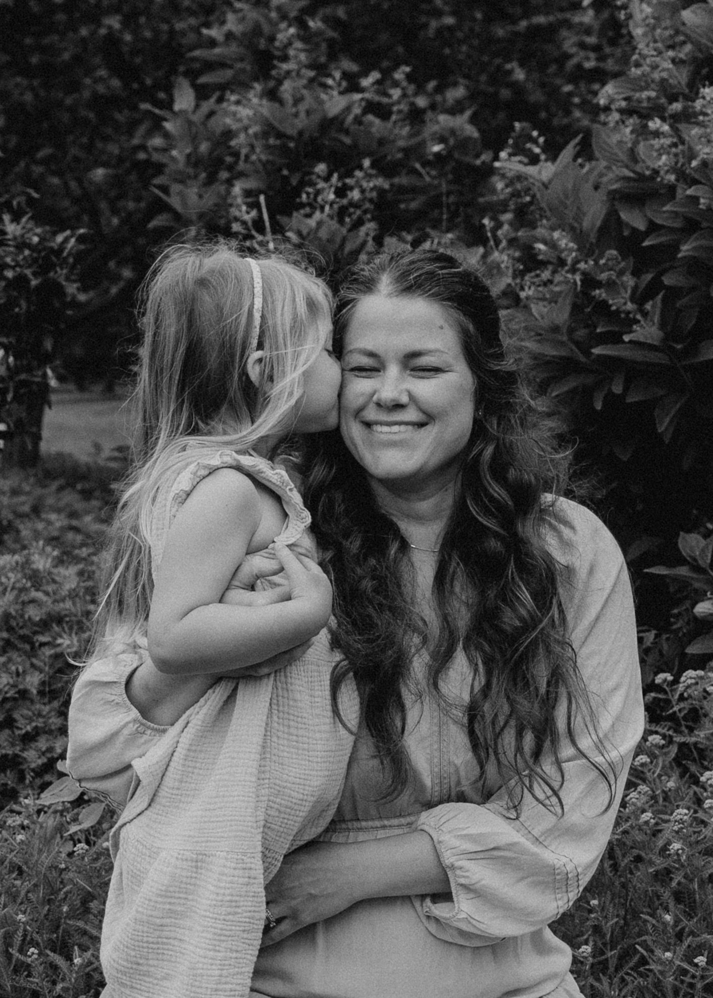 Black and white photo of a laughing mother holding her young daughter who kisses her cheek. Will Rogers Gardens family photos