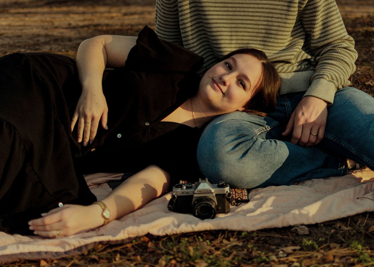 Woman lying on blanket outdoors with vintage camera and partner beside her. Couple photoshoot in Oklahoma City