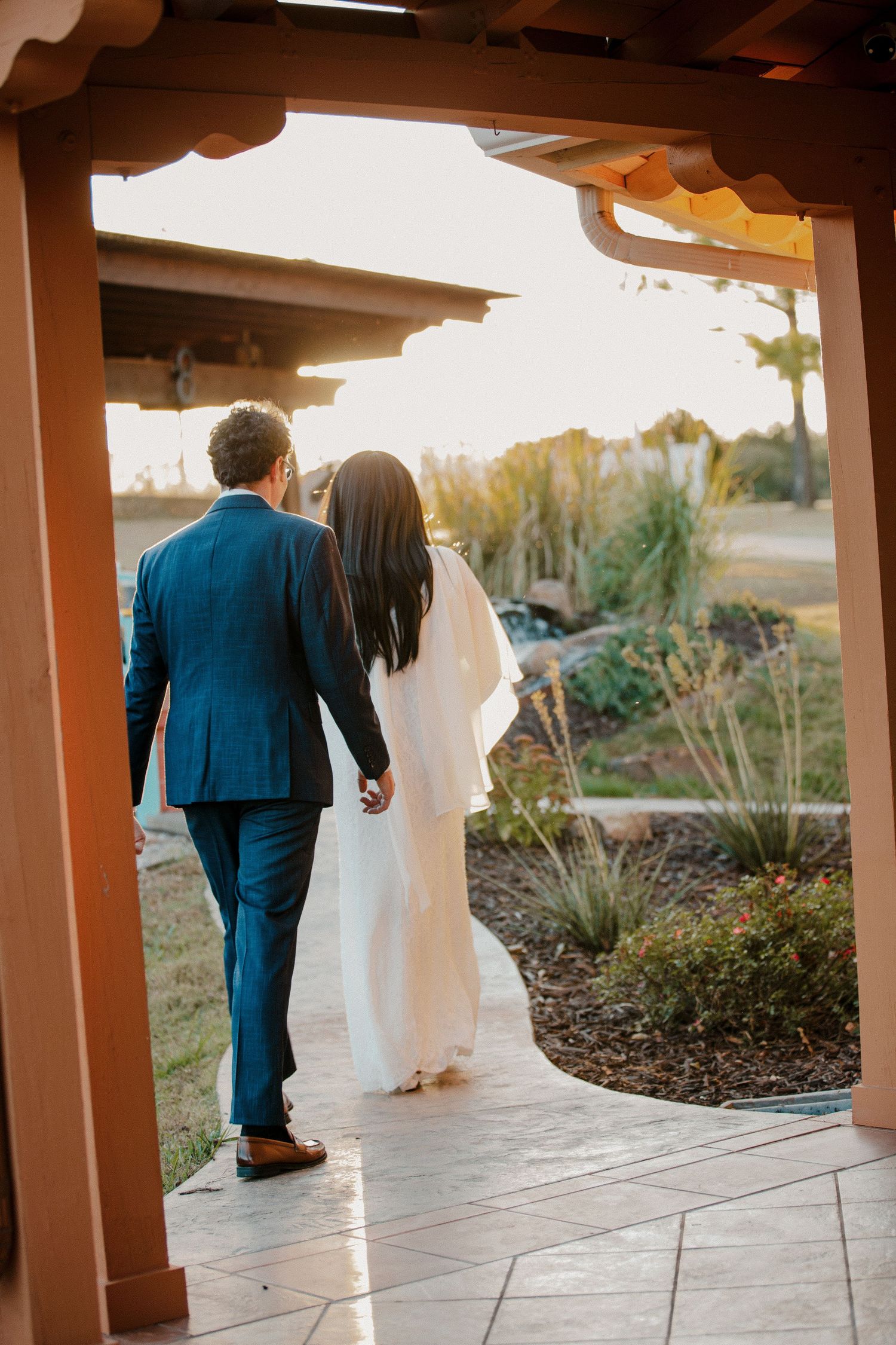 Newlywed couple walking hand in hand through a pergola at golden hour after their wedding. Oklahoma City intimate fall wedding.