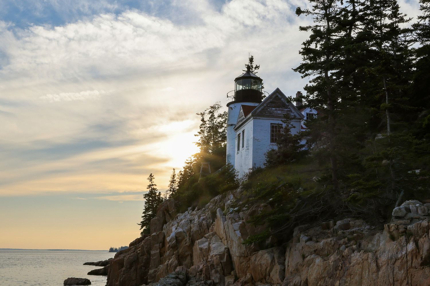 Bass Harbor Head Lighthouse glows in warm sunset light above the rocky Maine coastline.