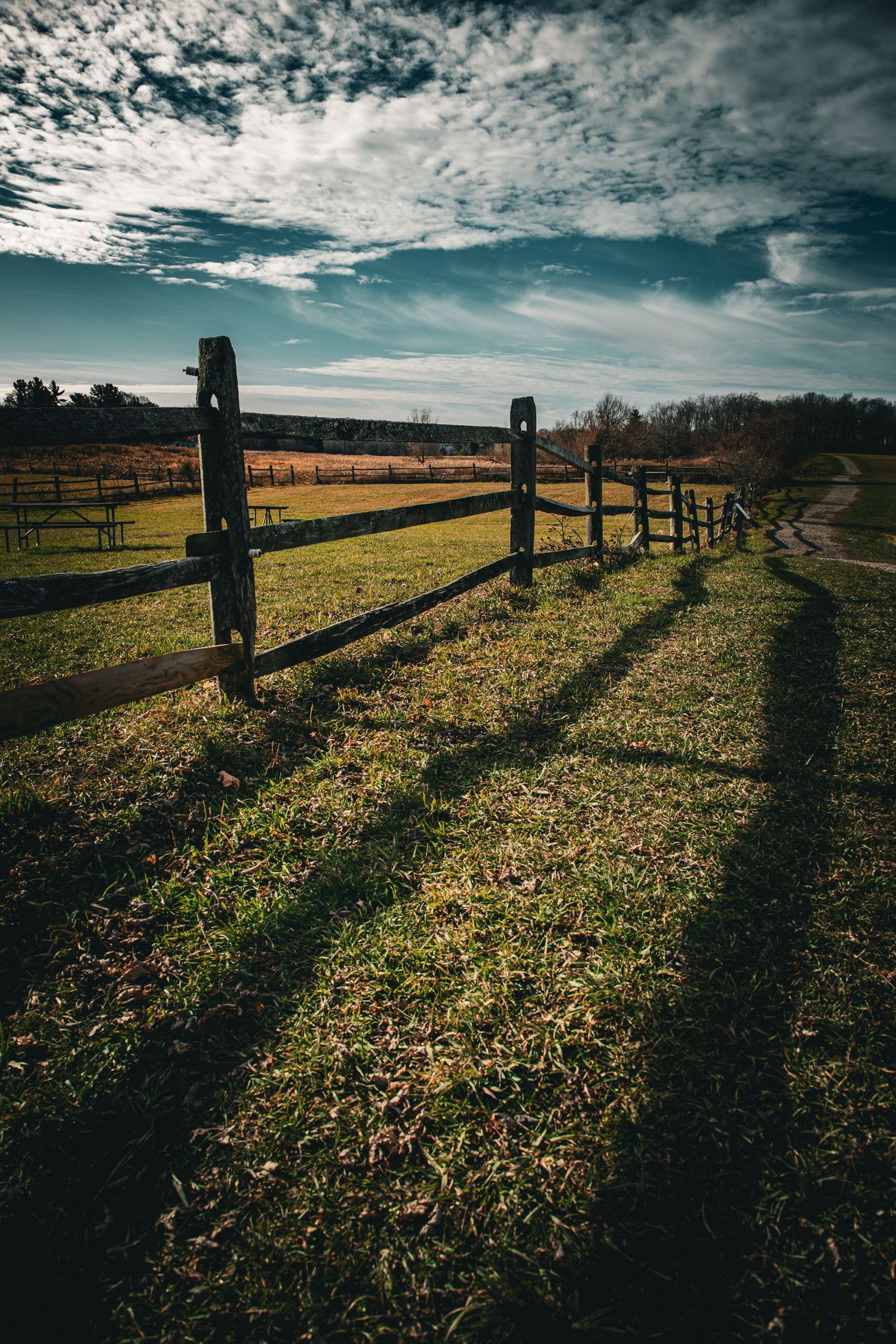 Rustic wooden fence casting long shadows on green grass field under dramatic cloudy sky at golden hour.