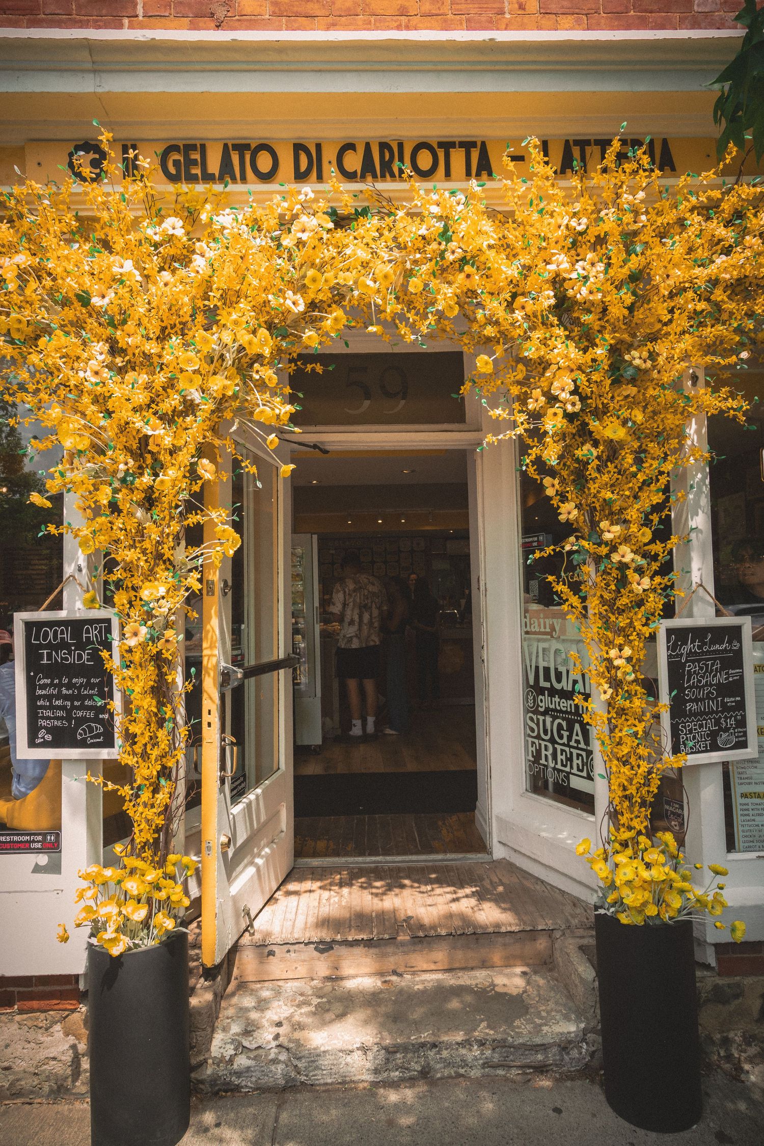 Charming gelato shop entrance adorned with yellow and white flowering branches in summer.