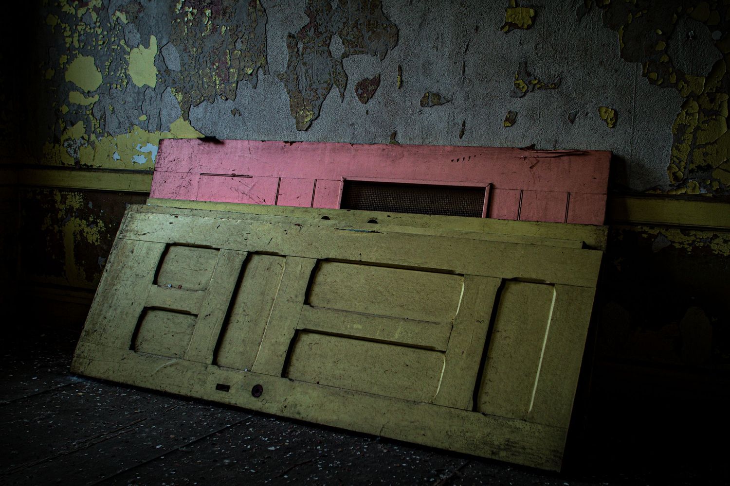 Two old painted wooden doors leaning against a deteriorating wall in an abandoned building.