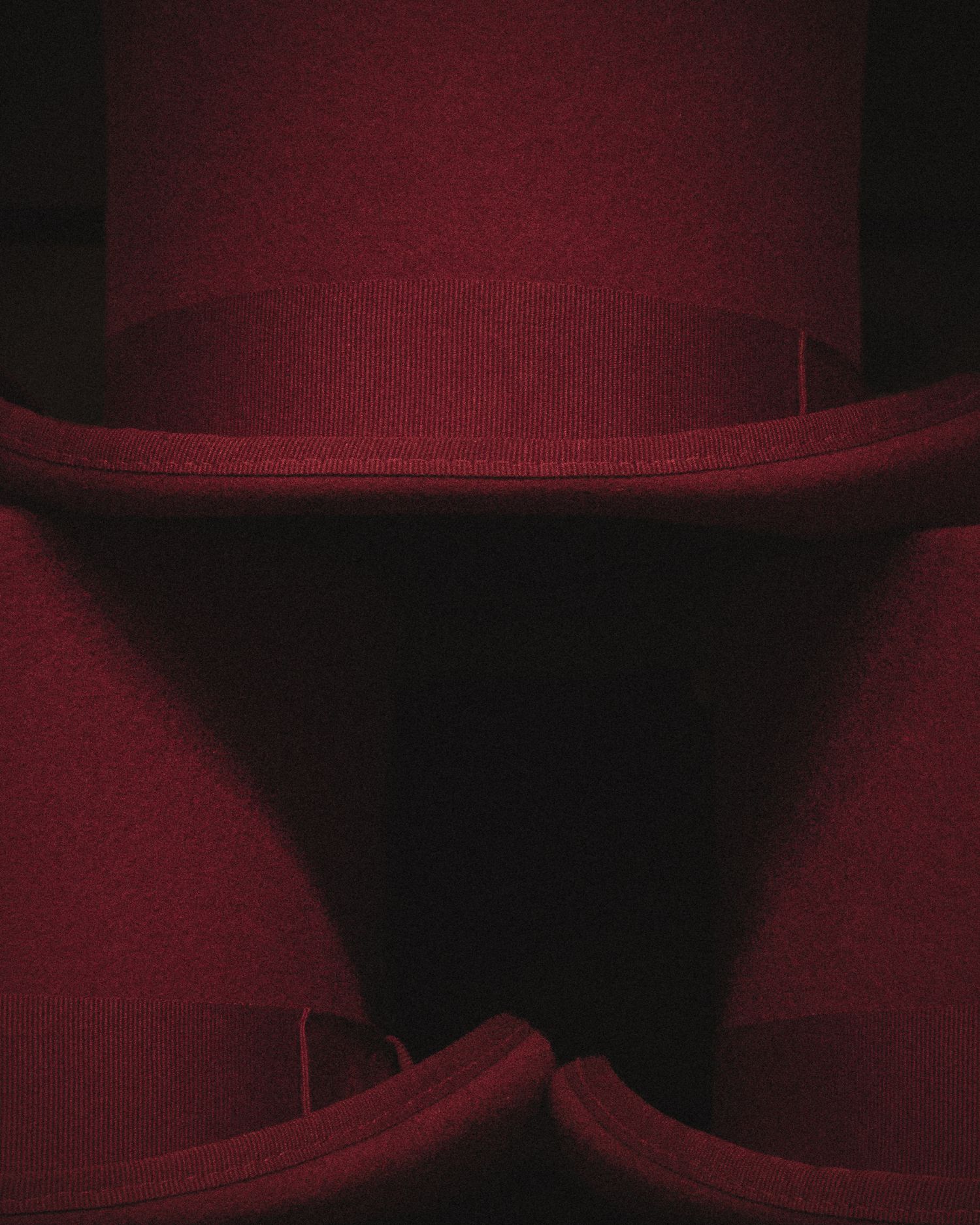 Close-up of stacked dark red felt top hats with dramatic moody lighting and shadows.
