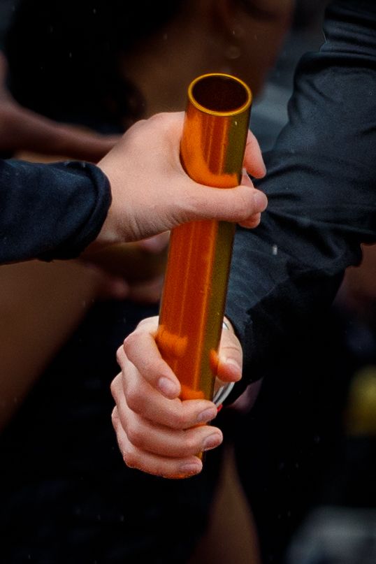 Two athletes exchange an orange relay baton during a track and field relay race competition.