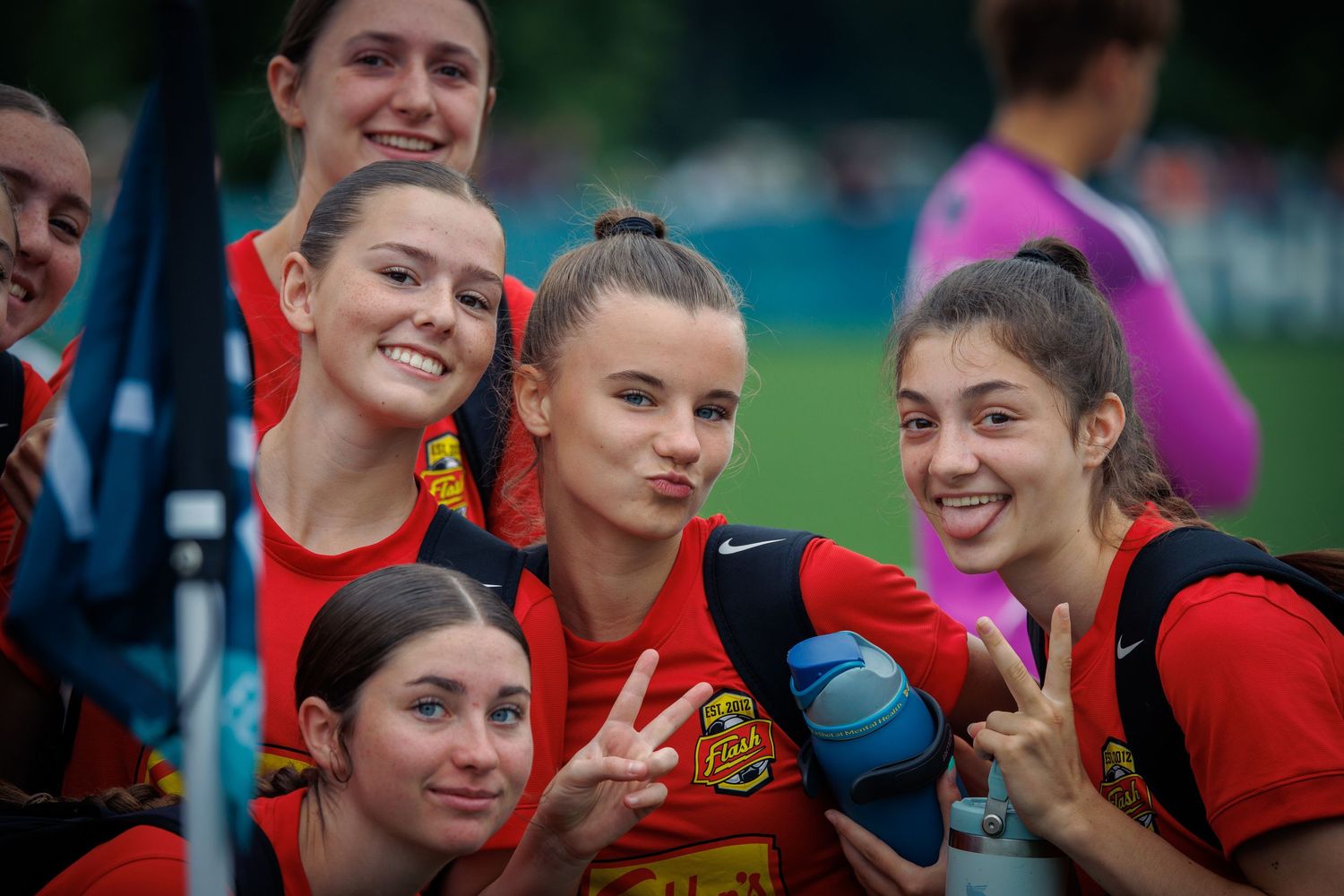 Female youth soccer players in red uniforms smile and pose together outdoors at a tournament.