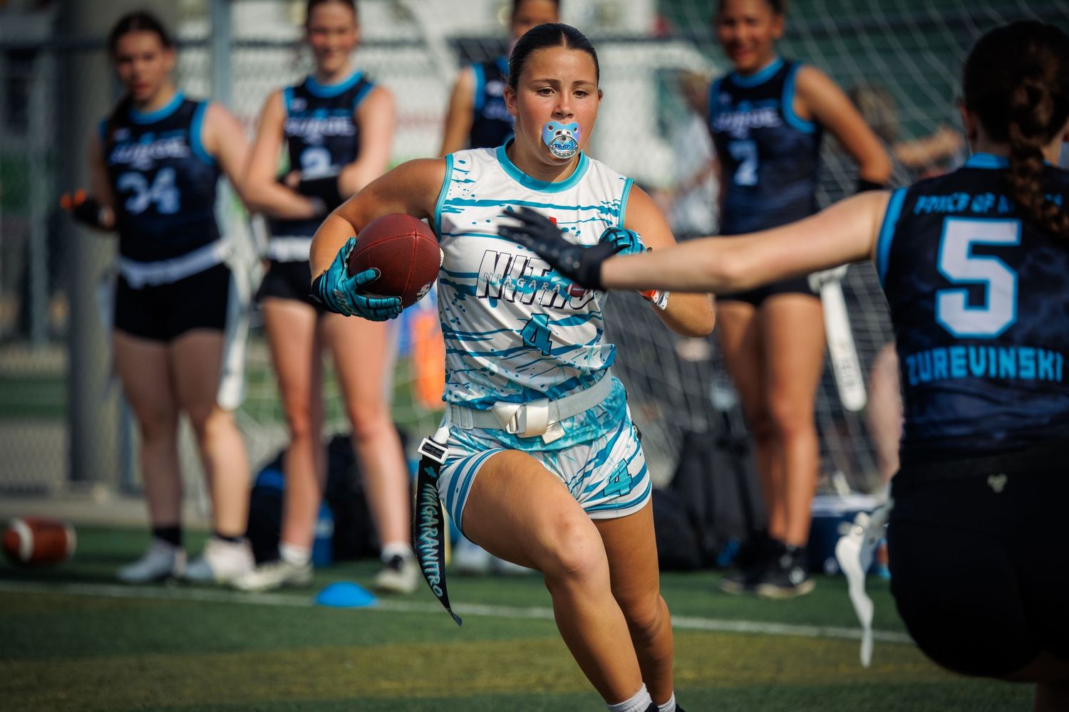 Female flag football player runs with ball during competitive women's league game outdoors.