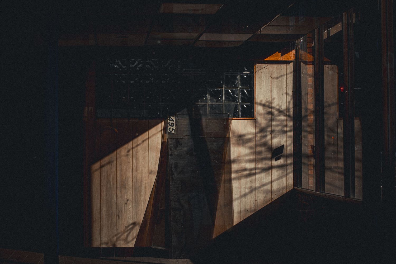 Dramatic shadows cast through wooden lattice window onto rustic wall in dark architectural space.