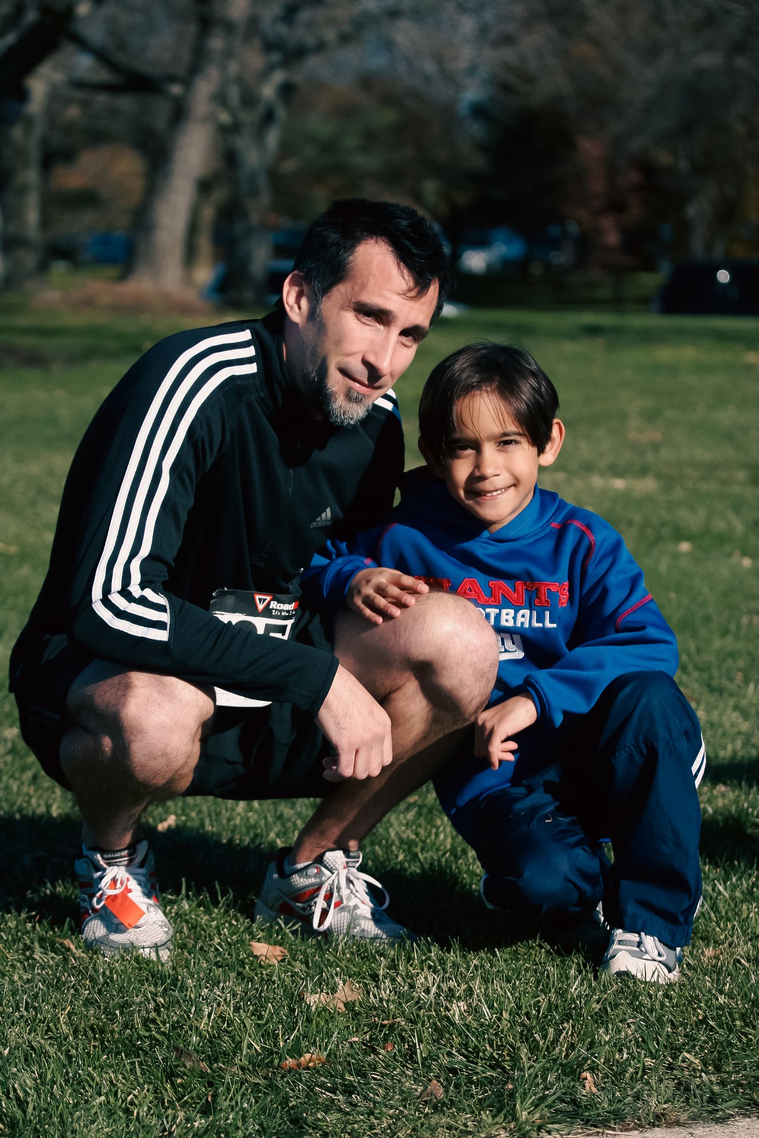 Adult man and young boy posing together outdoors on grass in a park.