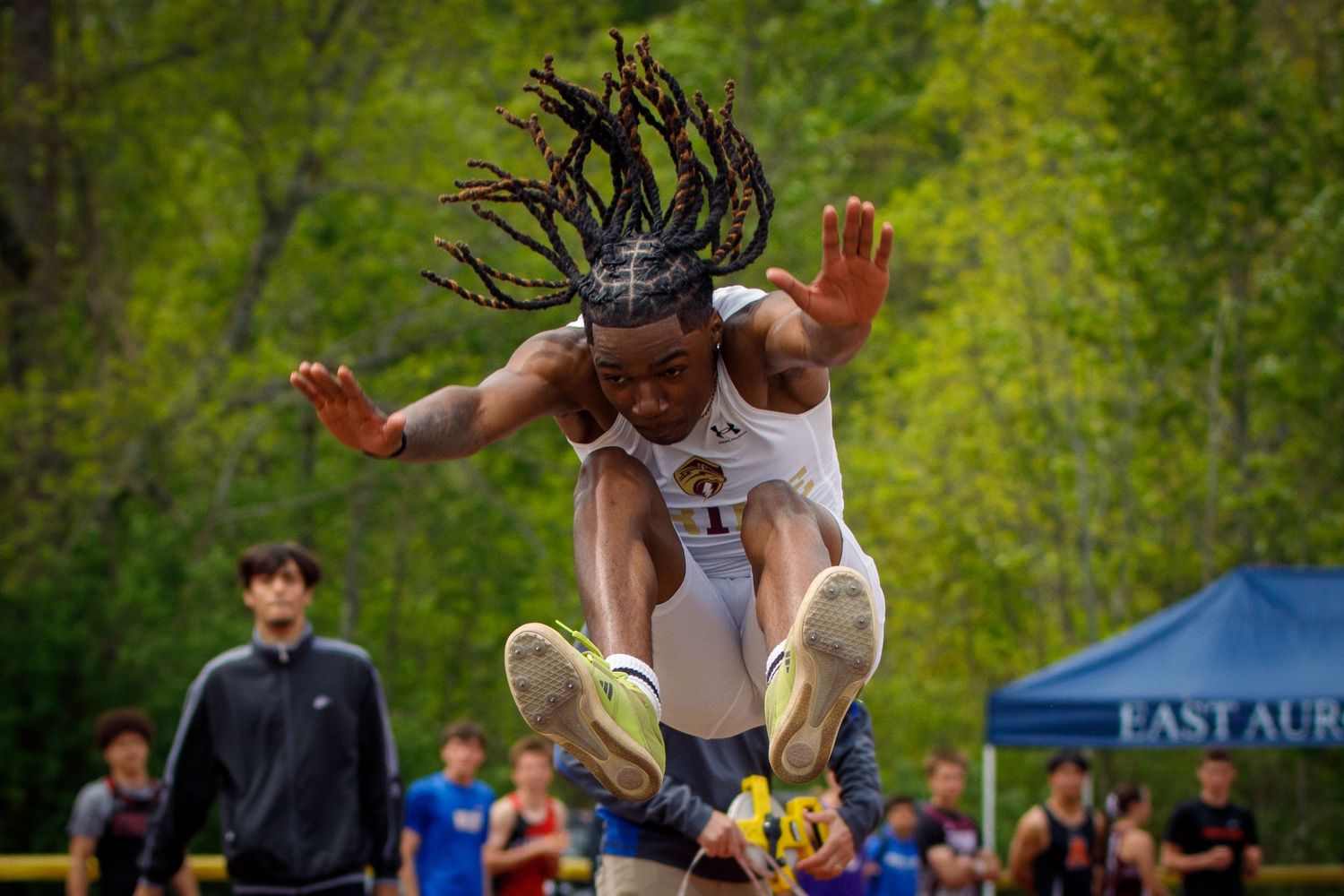 An athlete performs an impressive long jump, soaring through the air at an outdoor track and field competition.