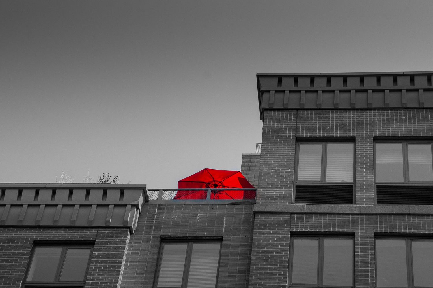 Selective color photo of a bright red umbrella on a rooftop terrace of a gray brick building.