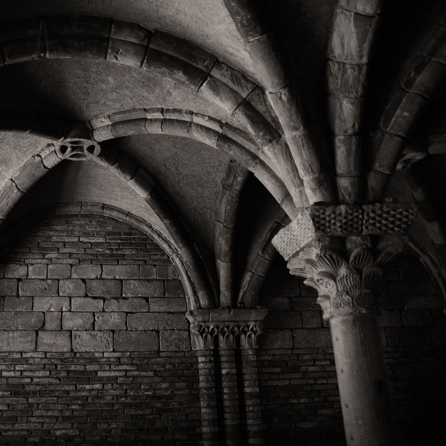 Black and white photo of medieval stone arches and ornate carved columns in a historic crypt.