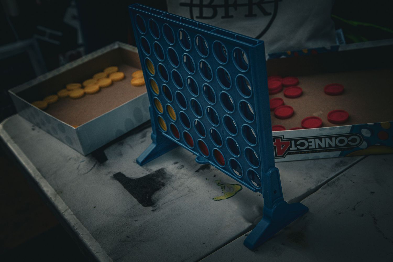 Blue Connect Four board game on a table with scattered red and yellow game pieces.