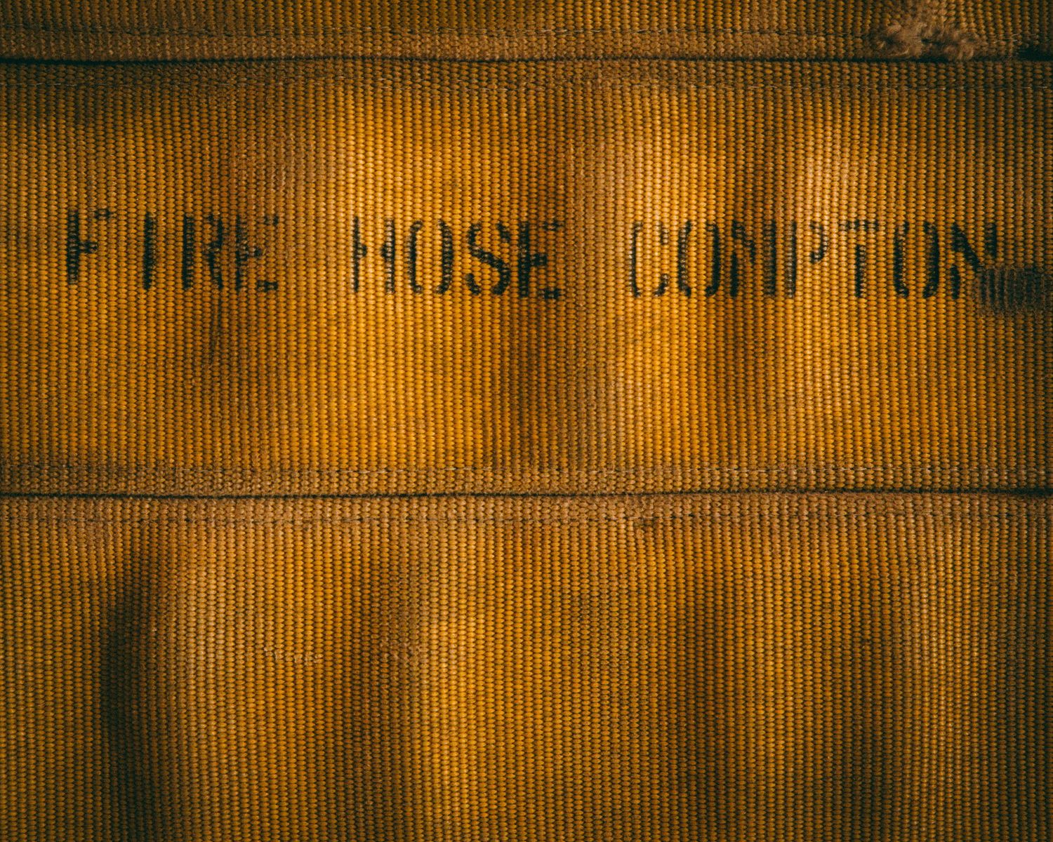 Close-up of aged yellow canvas fire hose with stenciled text reading Fire Hose Compton.
