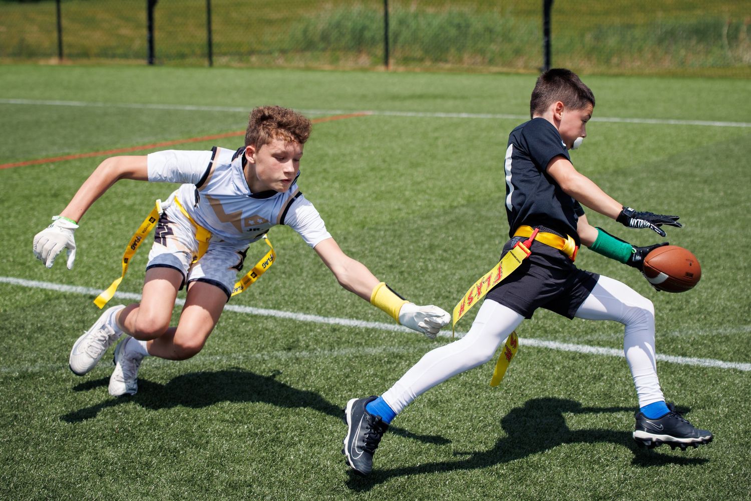 Two young boys compete in a flag football game as one player attempts to pull the flag of the ball carrier.