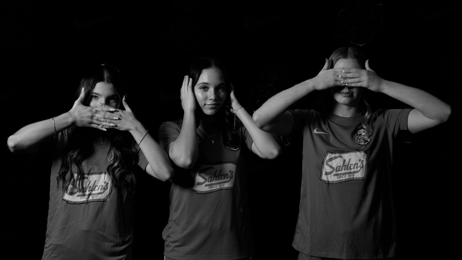 Three female soccer players recreate see no evil, speak no evil, hear no evil pose in black and white.