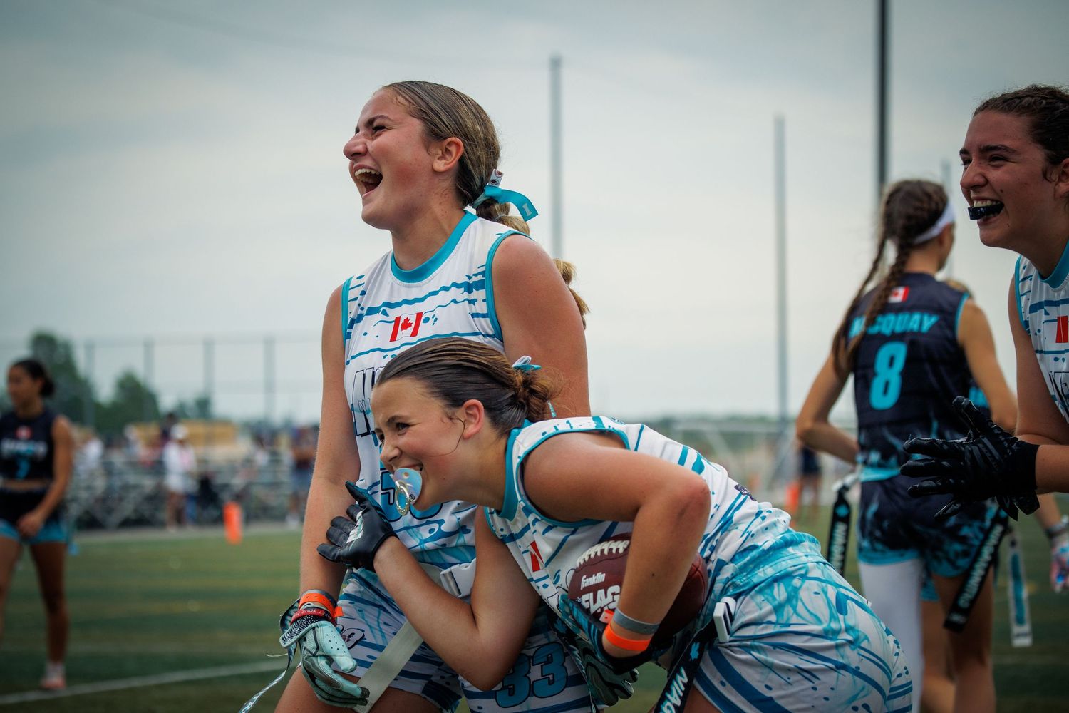 Excited female athletes in tie-dye uniforms celebrate joyfully on a football field during a game.