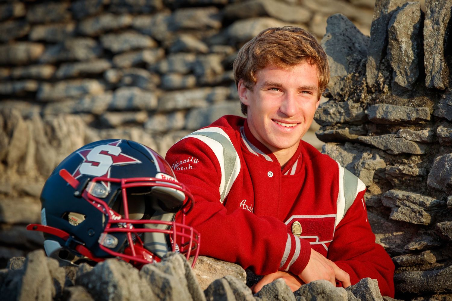 High school senior portrait with varsity jacket and football helmet
