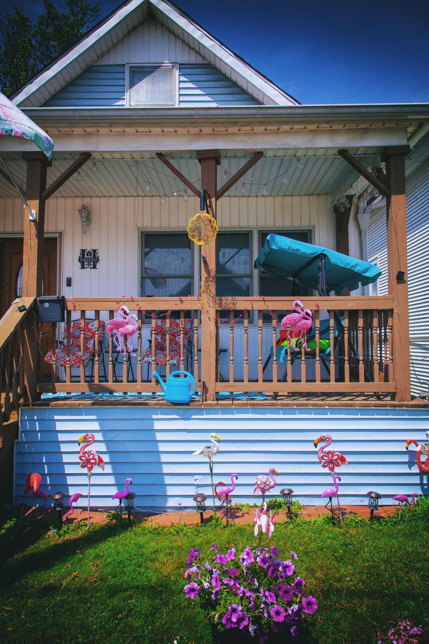 Colorful suburban house porch decorated with pink flamingo ornaments, flowers, and cheerful summer decorations.