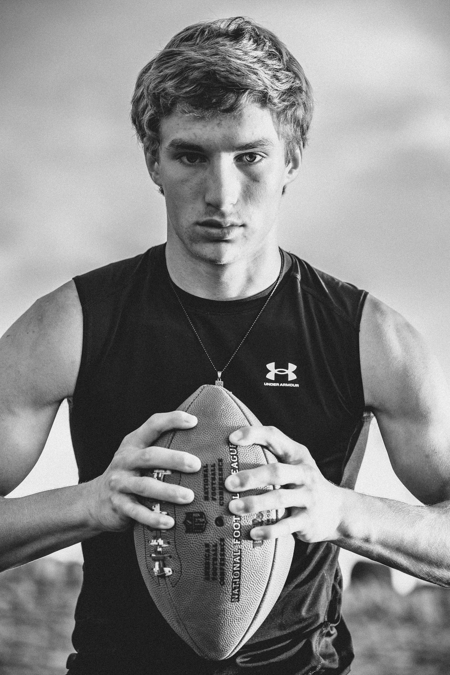 High school football player holding a football at sunset