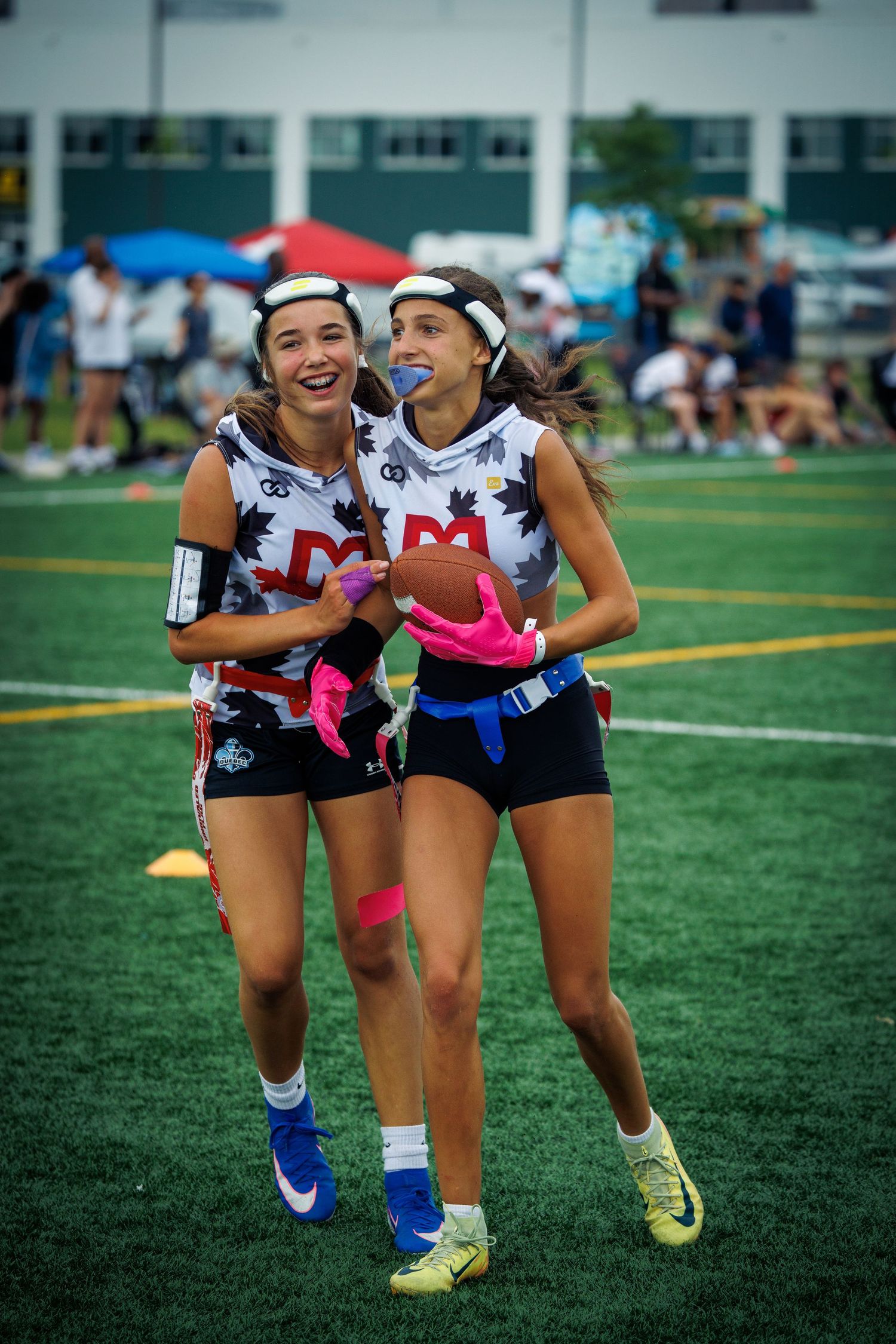 Two smiling female flag football players in matching uniforms share a fun moment on the field.