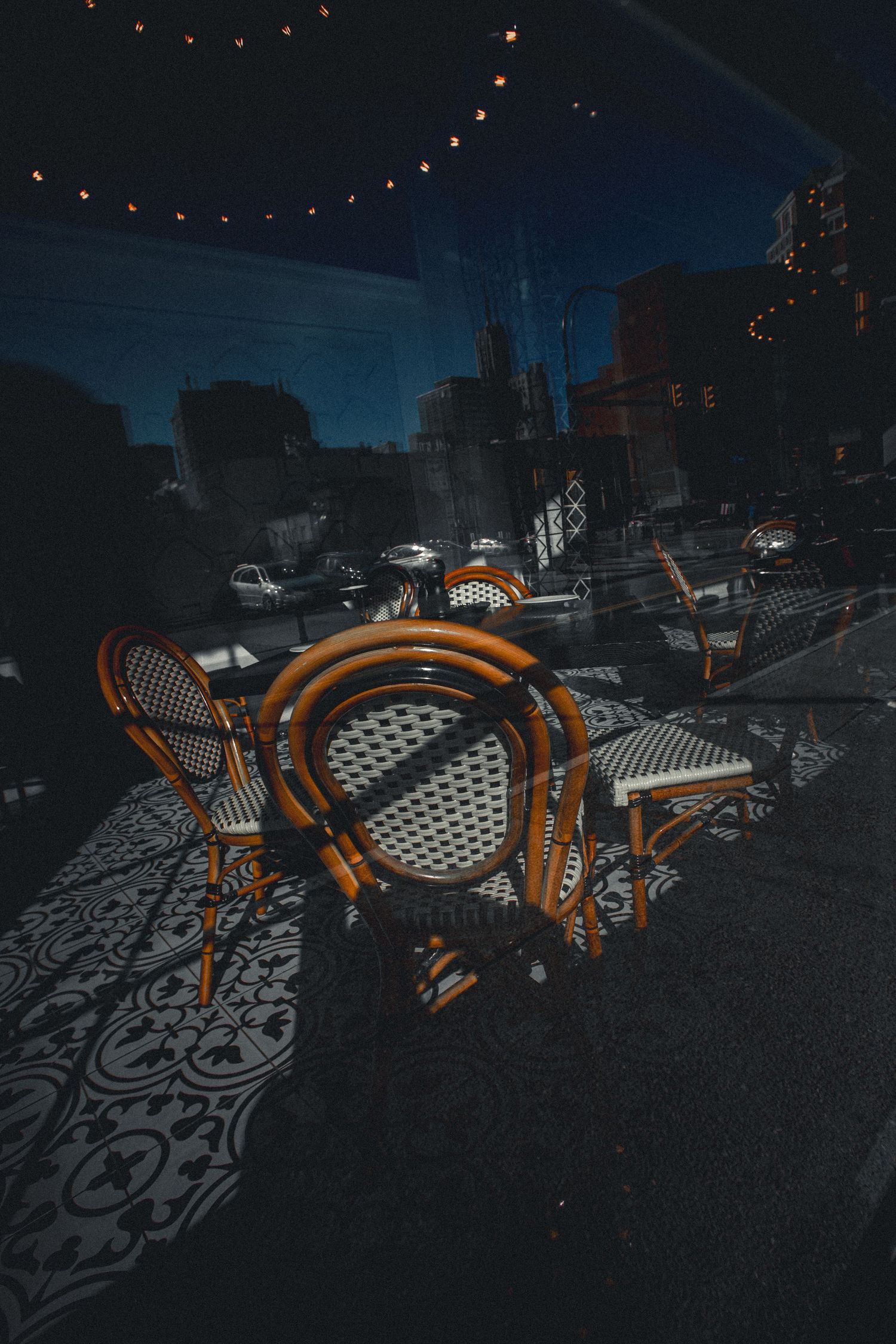 Moody cafe interior with wicker chairs and patterned floor reflected in window at dusk.