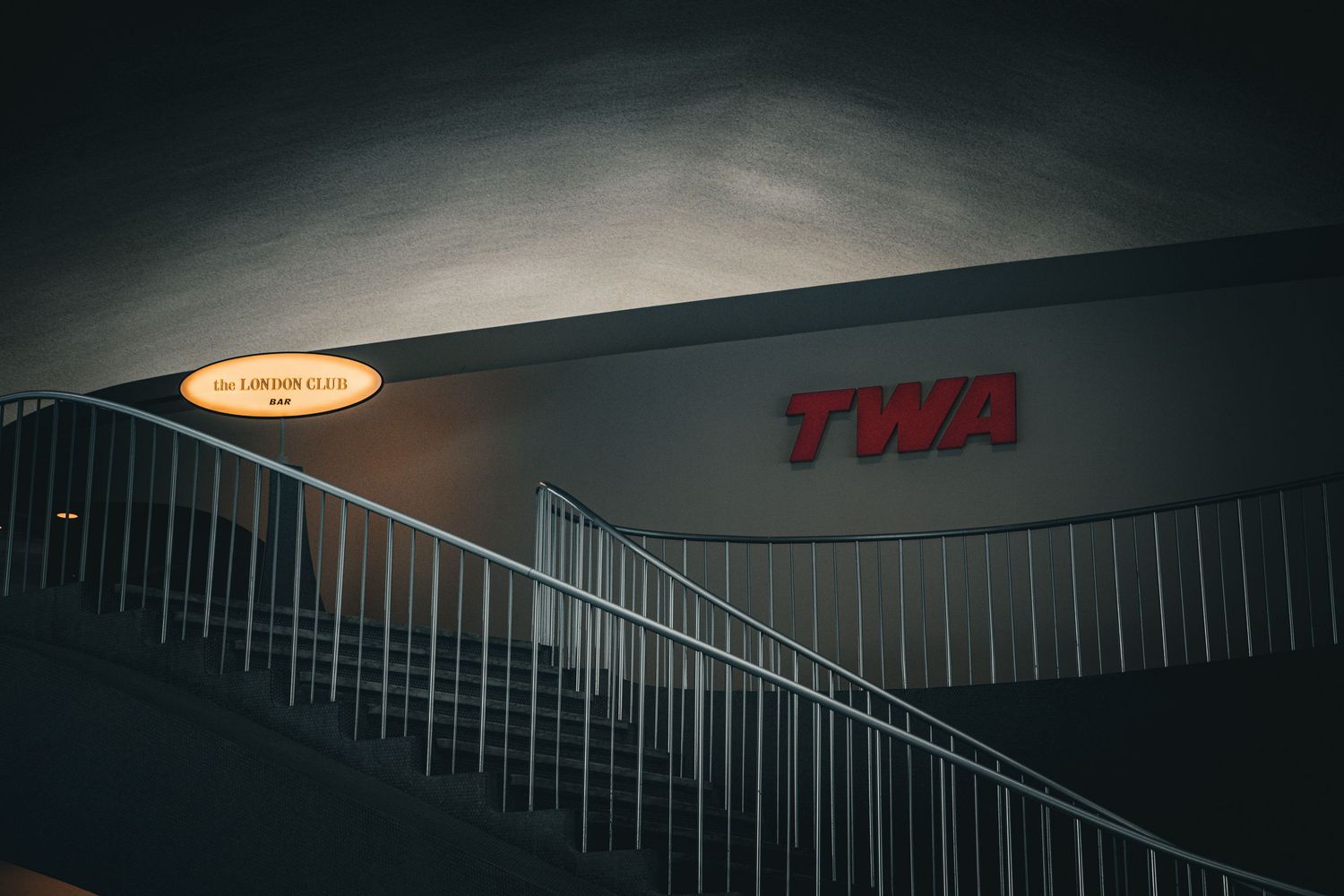 Illuminated red TWA sign on a dark building exterior with metal staircase railing at night.