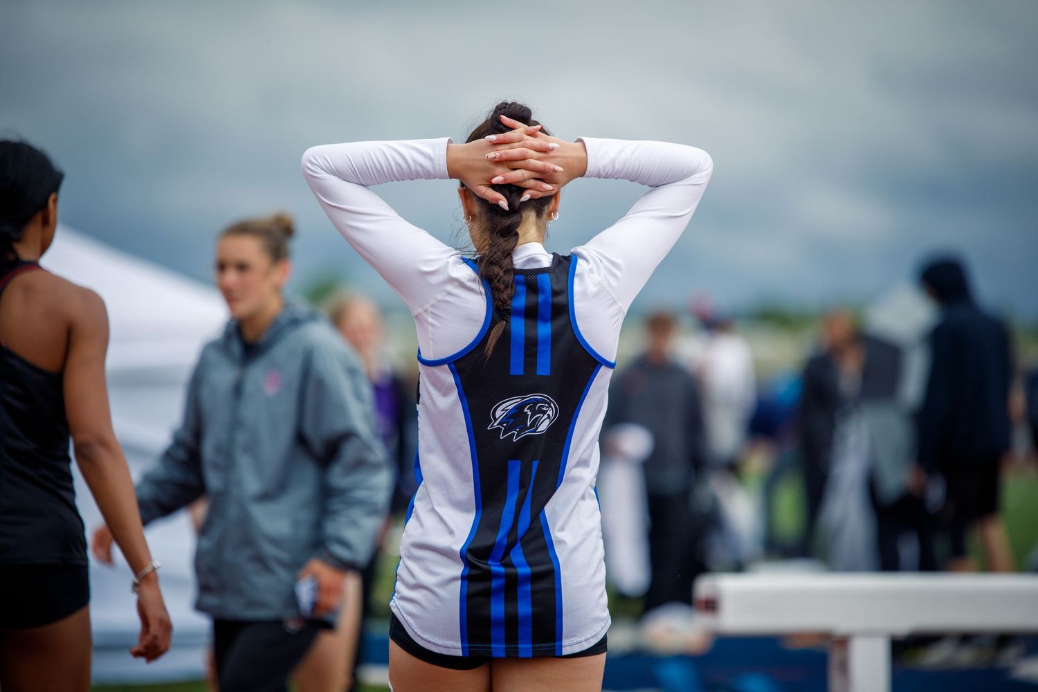 Female track and field athlete stands with hands behind her head after competing at an outdoor meet.