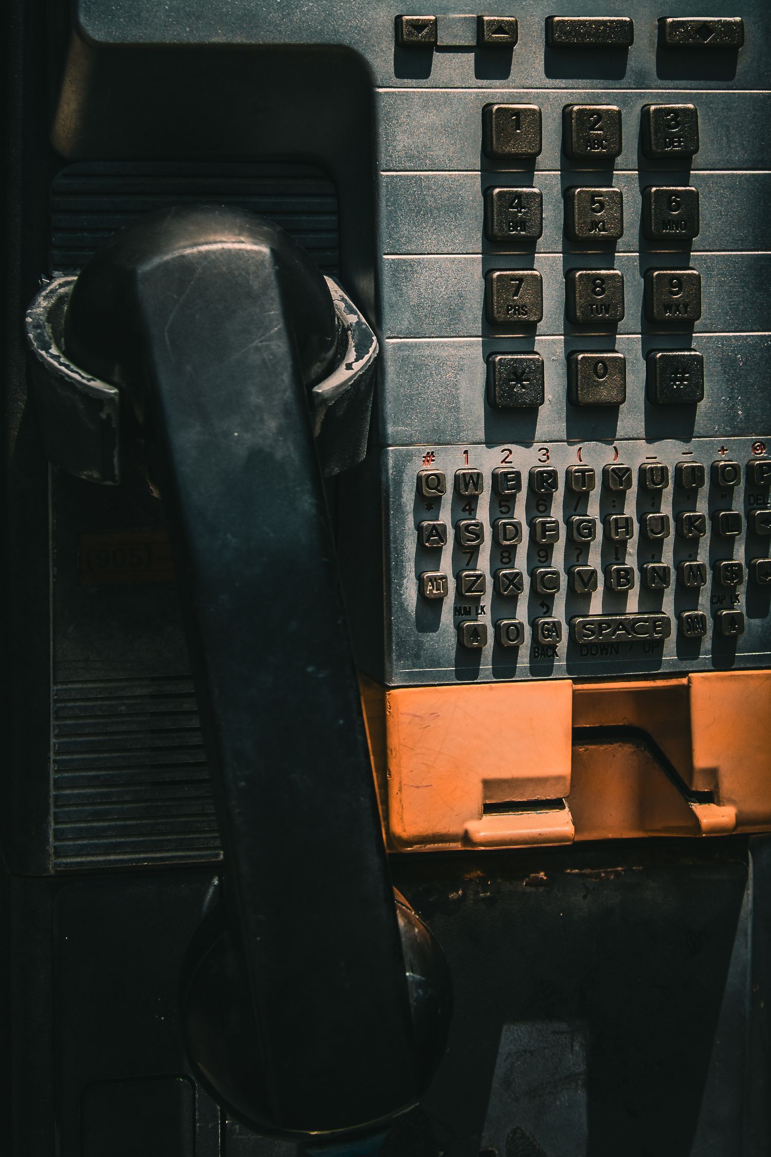Vintage black payphone with alphanumeric keypad and worn orange coin slot in dark setting.