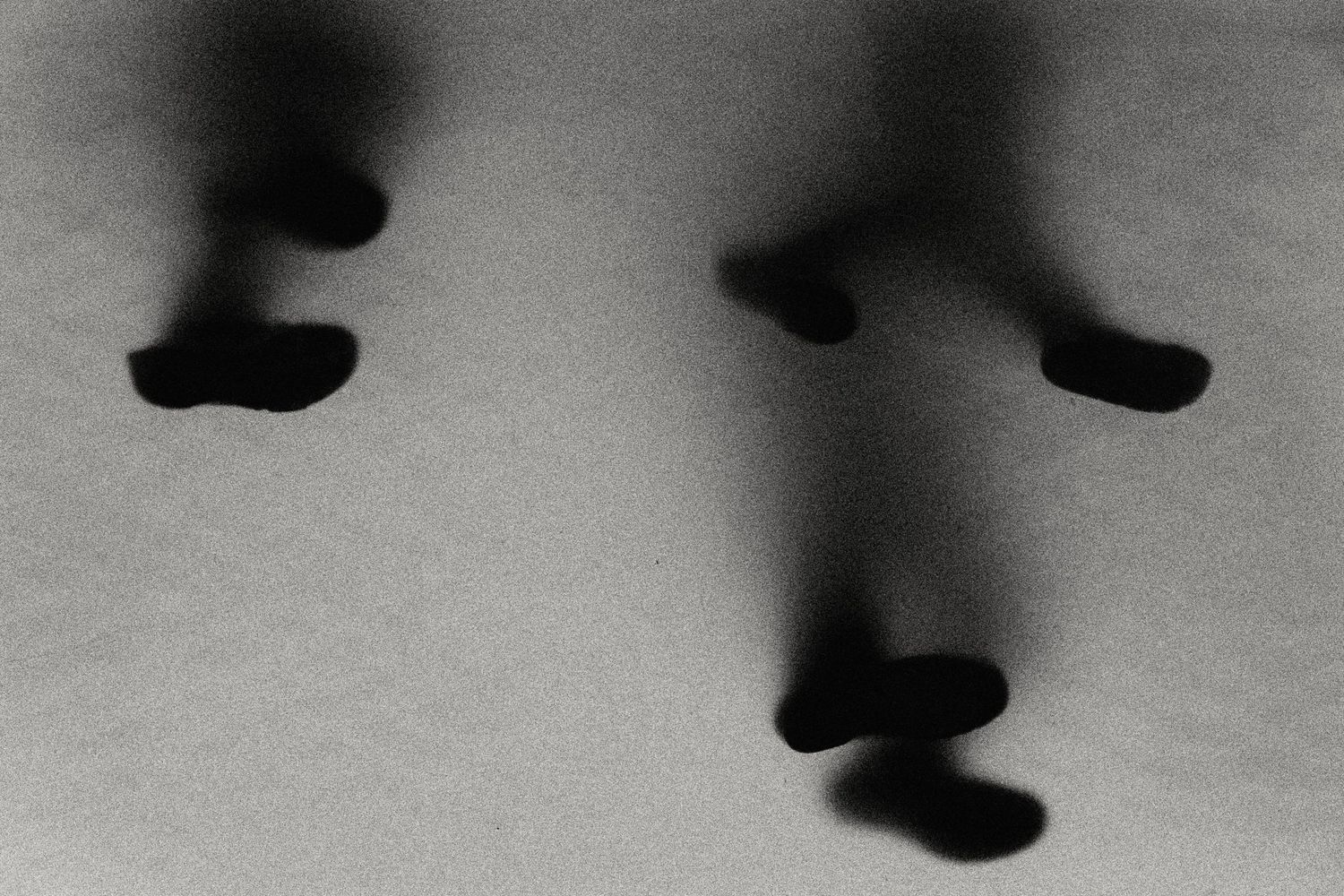 Abstract black and white photograph of blurred human foot shadows on light gray surface.