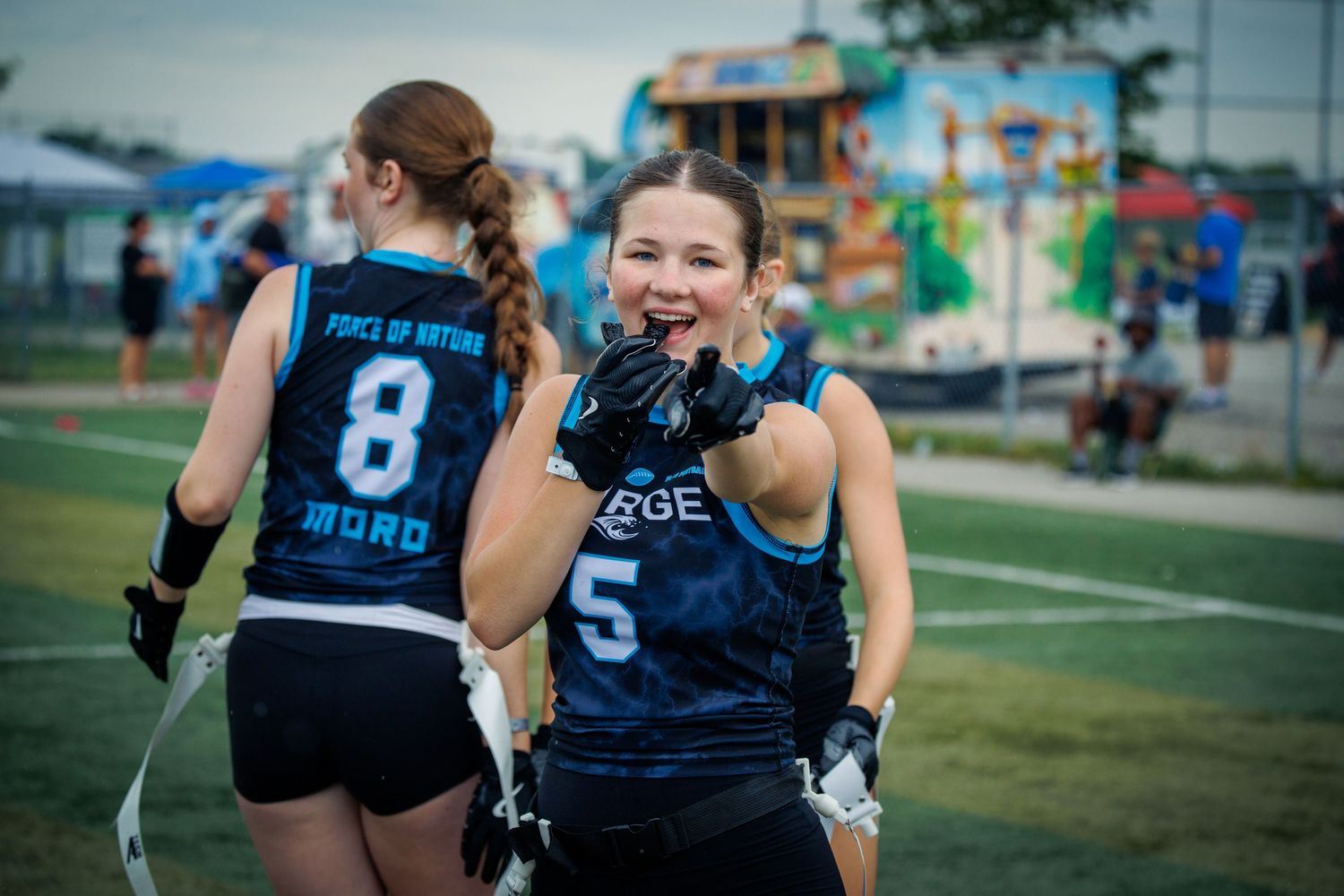 Smiling female flag football player in blue #5 jersey celebrating on field.