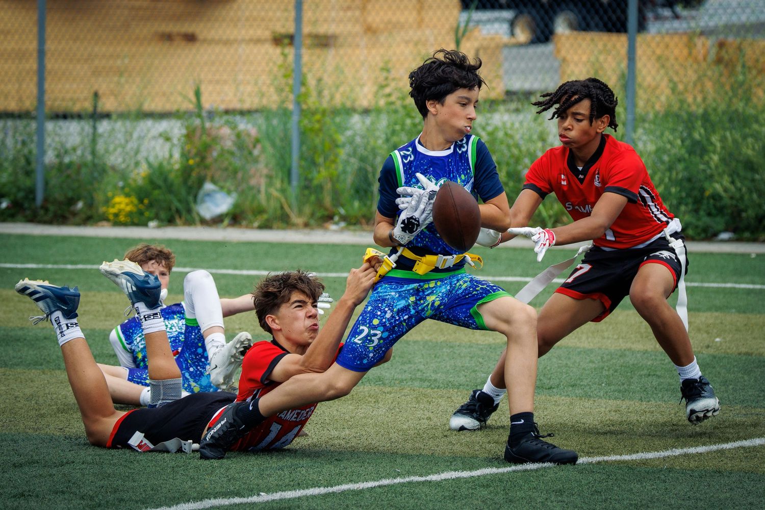 Young players compete in a flag football game, with one player diving to make a catch on a green turf field.