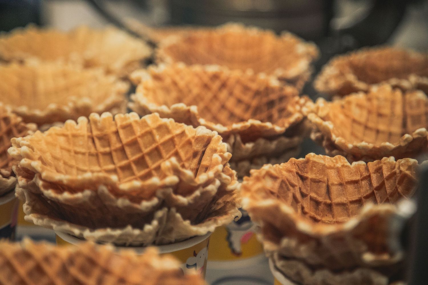Freshly baked golden waffle ice cream cones cooling in rows at a bakery or ice cream shop.