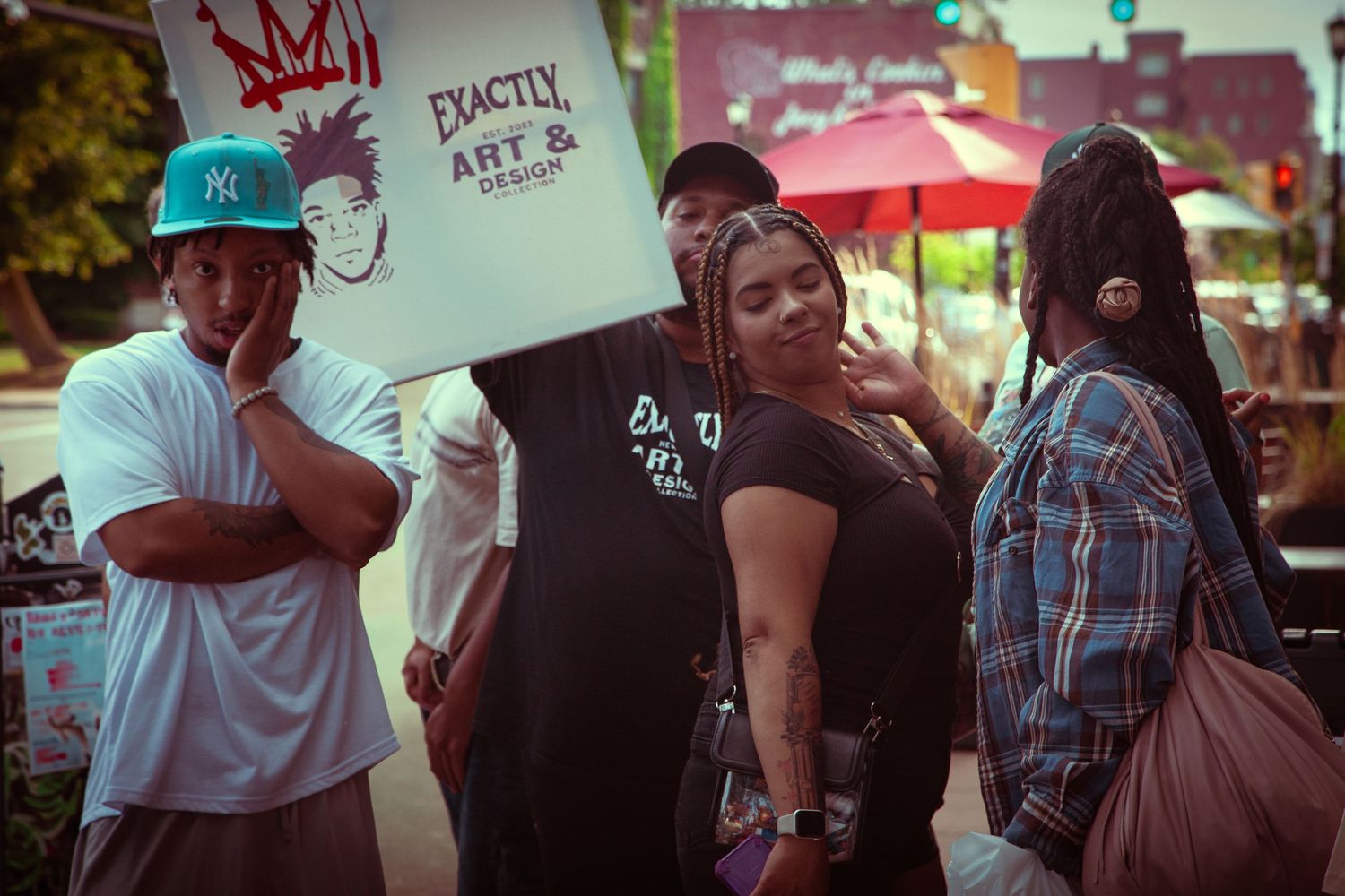 Group of people standing on urban street corner near an art and design promotional sign.
