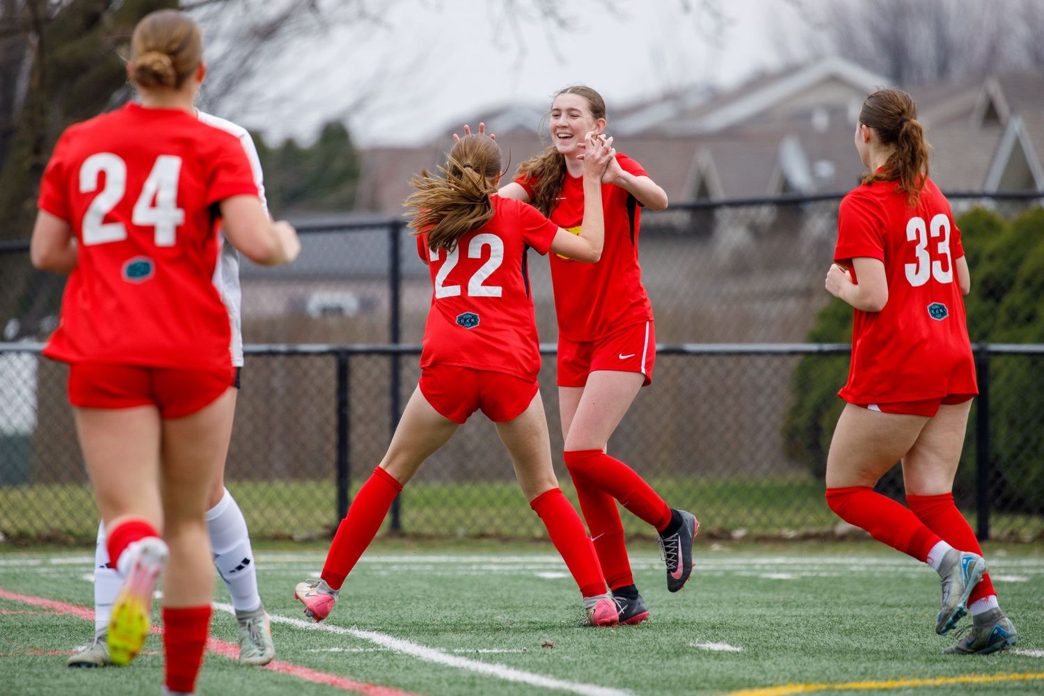 Girls in red soccer uniforms celebrate together on the field after scoring a goal during a match.
