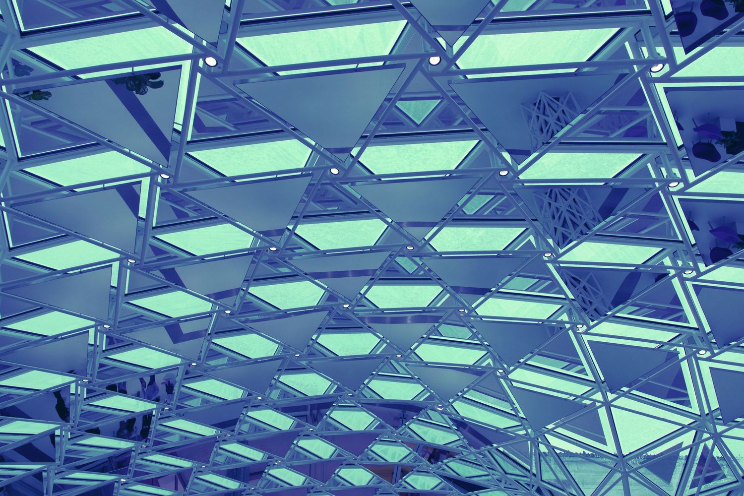 Abstract blue geometric ceiling with triangular mirrored panels and glowing LED light fixtures.