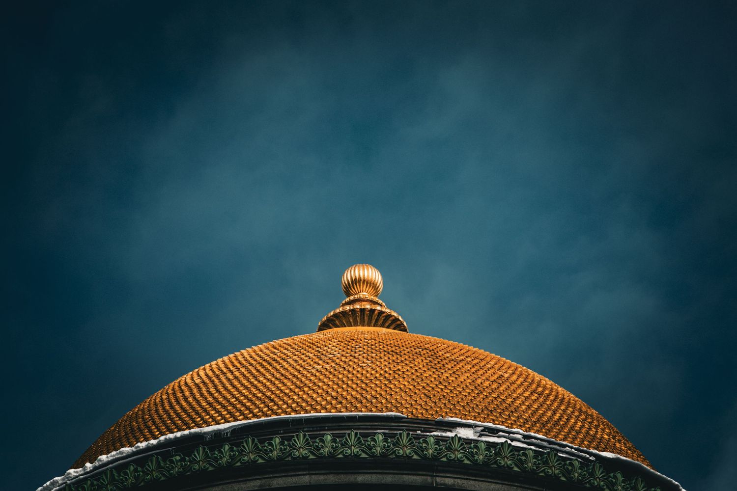 Golden ornate dome of historic building topped with decorative finial against moody dark blue sky.