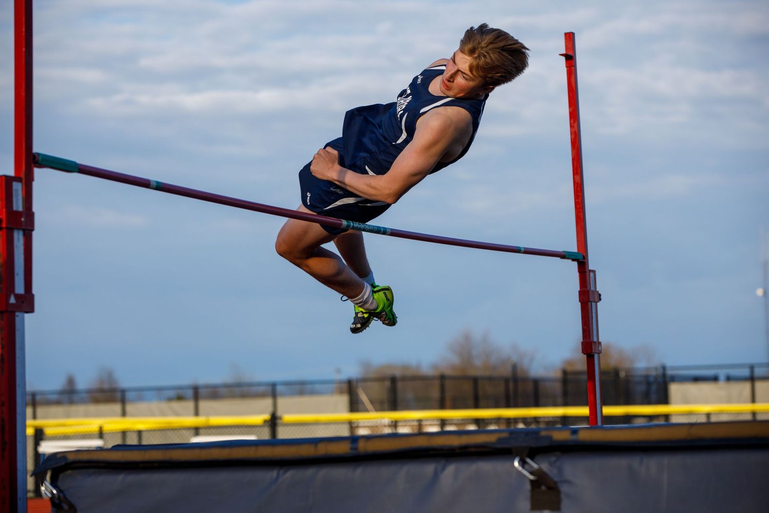 Male athlete performs a high jump, arching his back over the bar during an outdoor track and field competition.