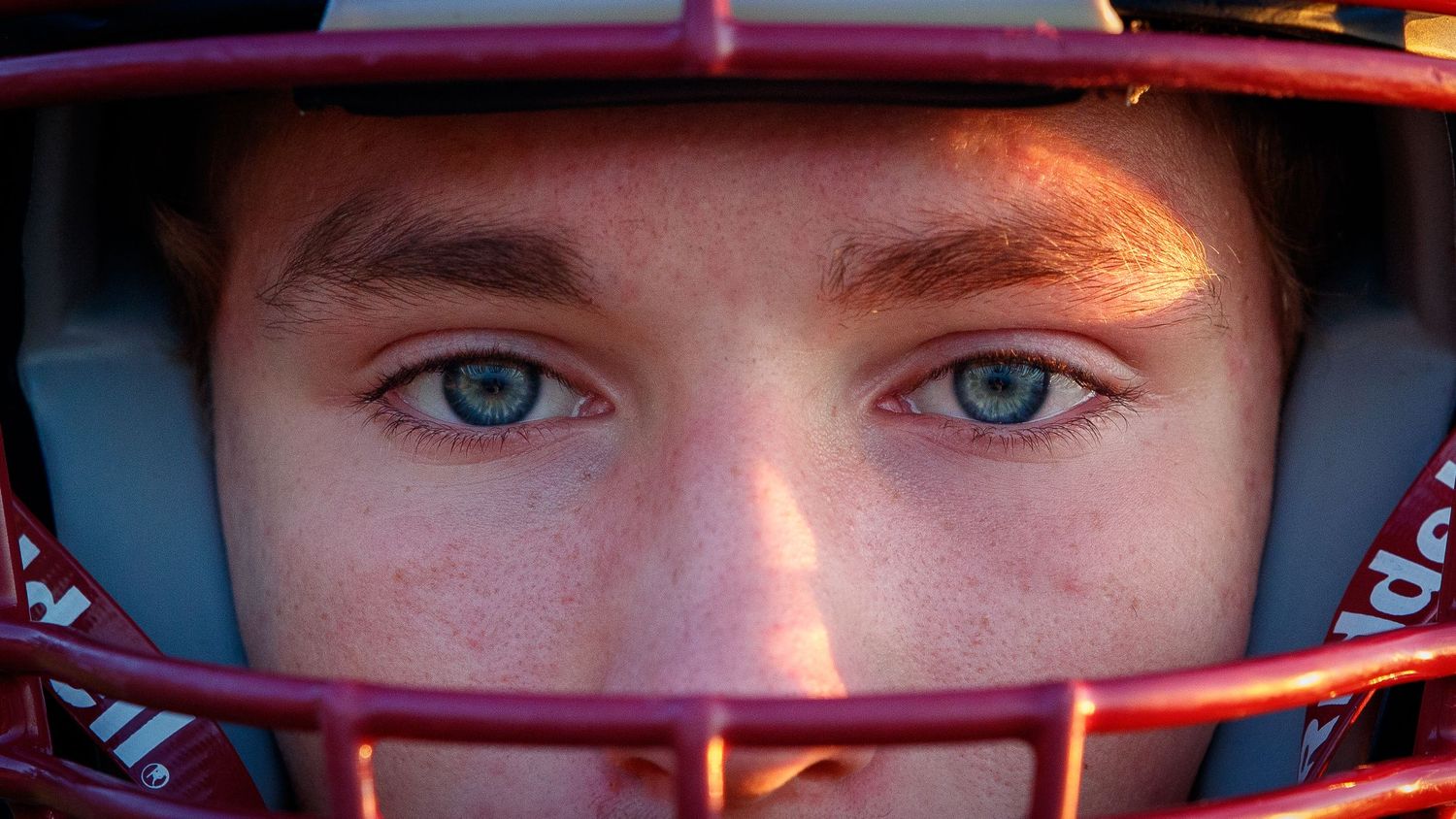 Close-up of a young athlete's blue eyes wearing a red football helmet with face guard.