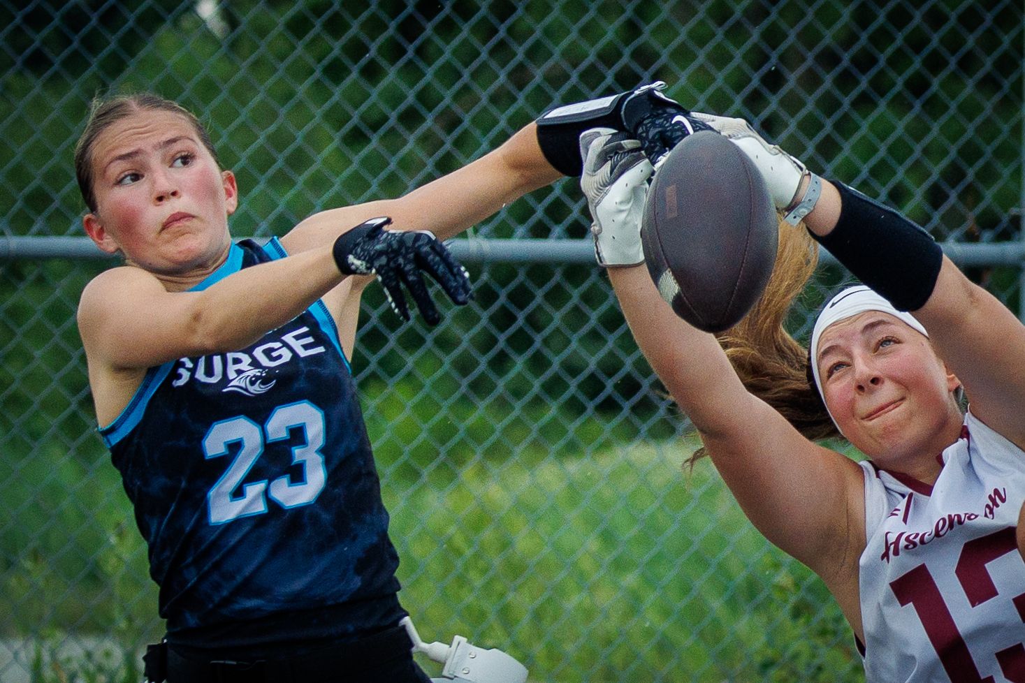 Female flag football player #23 in blue Surge jersey attempts to block a pass during an intense game.