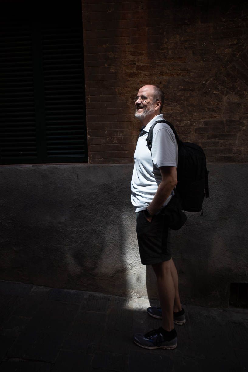 Black-and-white photo of a man standing in a narrow alleyway with a backpack