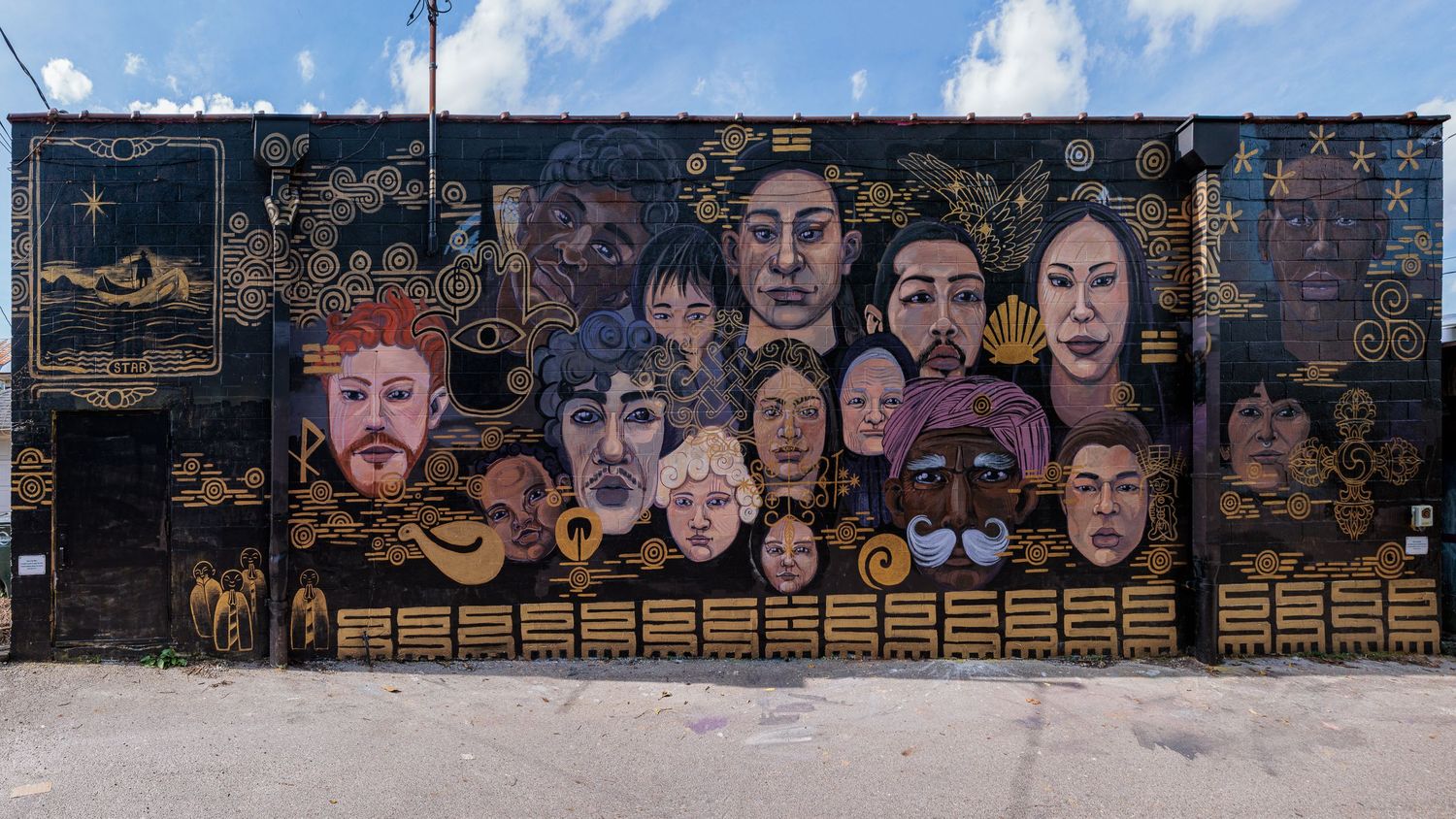 Wide street view of the full completed mural wall covered in painted faces