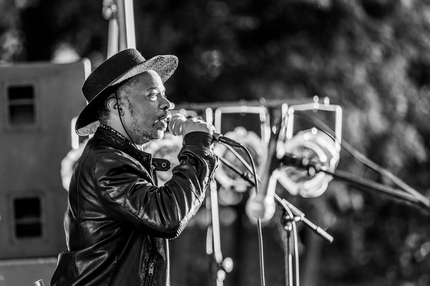 Black-and-white photo of a musician singing into vintage-style microphones, wearing a hat