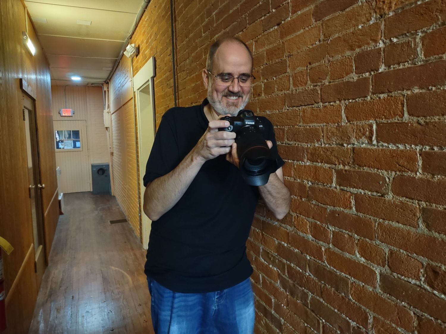 Karl Yost standing in a brick hallway holding up his camera