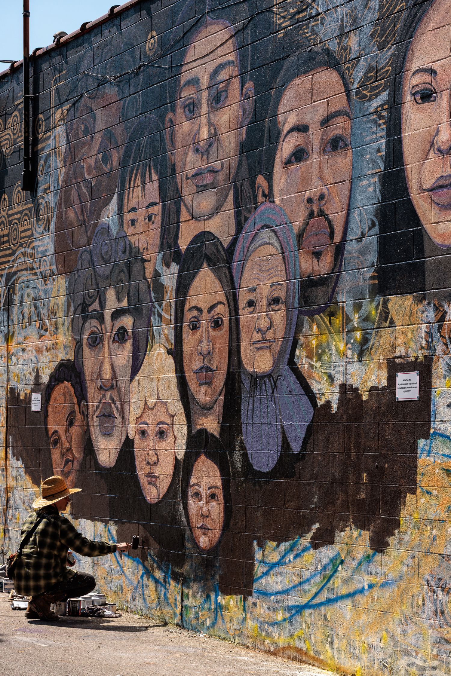 Muralist Pierre Nagley walking past a completed wall of painted faces