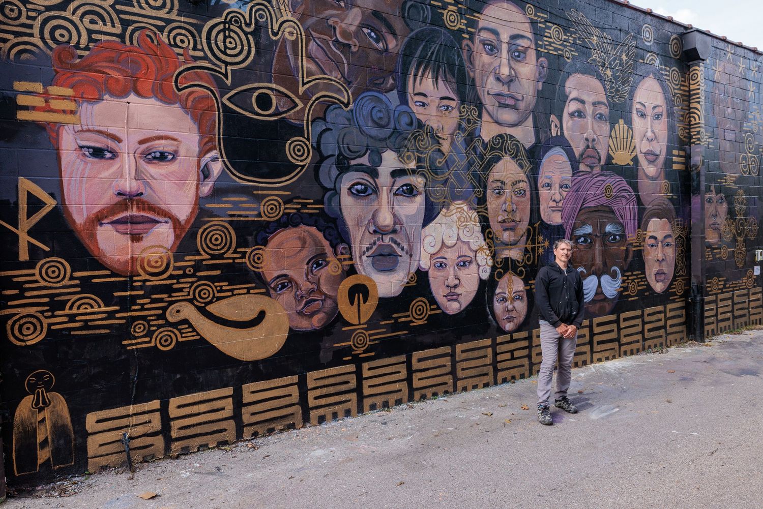 Wide view of a mural completed showing dozens of painted faces, with the Muralist Pierre Nagley