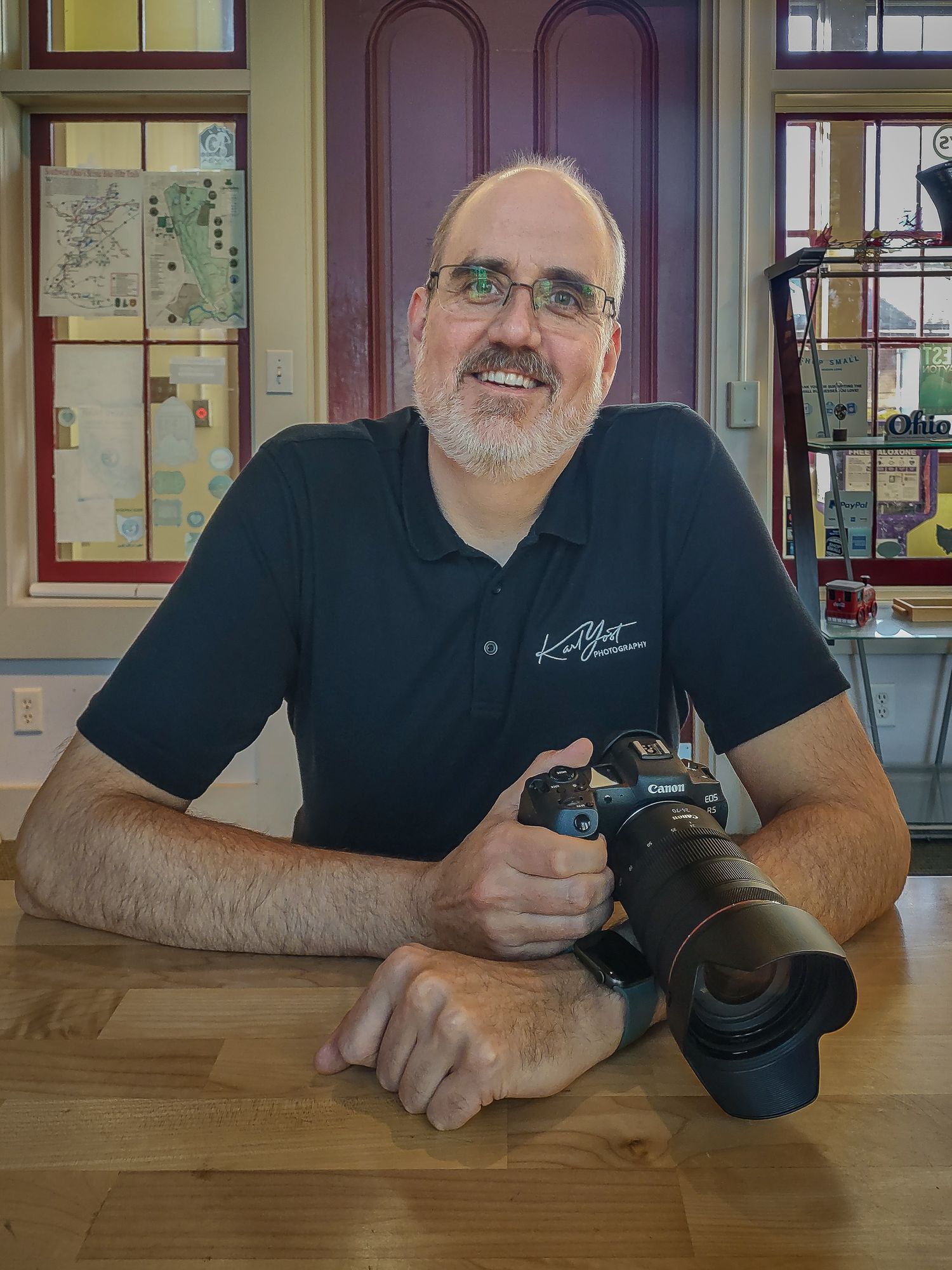 Karl Yost seated at a table holding his camera, colorful window in the background